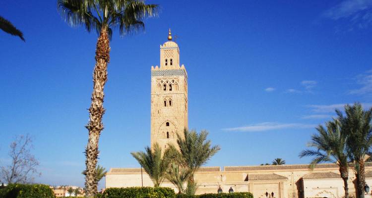 Koutoubia Mosque’s sandstone minaret framed by palm trees under a deep blue sky in Marrakesh.