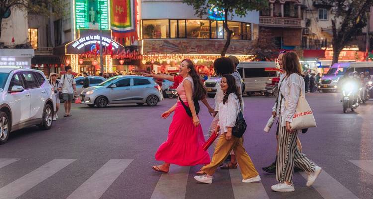 Vrienden in felle kleren steken 's avonds een druk kruispunt in Hanoi over onder neonlichten.