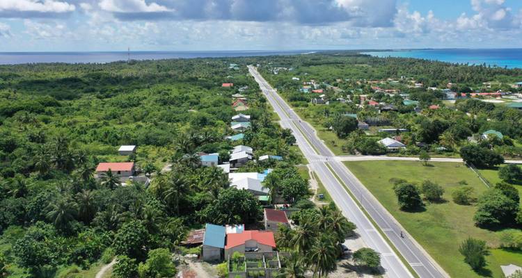 Aerial view of a narrow island road cutting through lush jungle with turquoise sea on both sides.