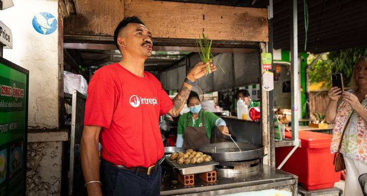 A street food vendor holding herbs in a market.