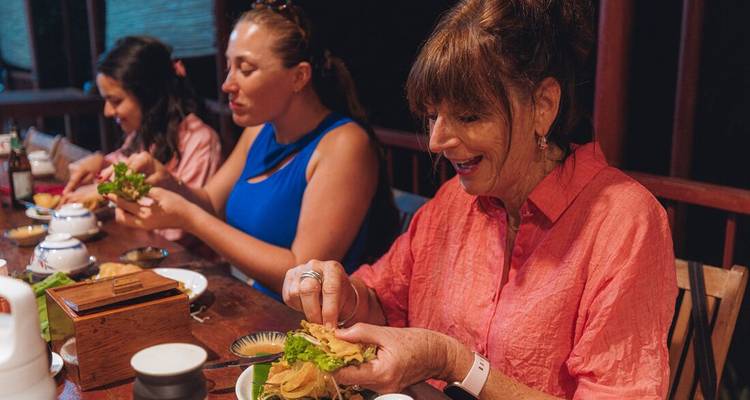 Les clients apprécient un repas local participatif autour d'une table en bois à l'intérieur du restaurant
