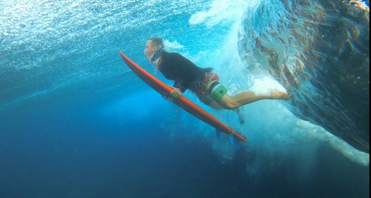 Vue sous-marine d'un surfeur effectuant un canard-plongée avec une planche rouge sous la surface de la vague.