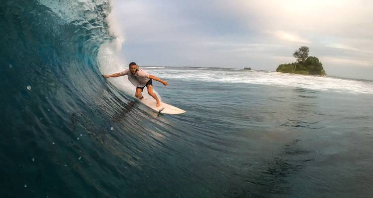 Un surfeur effectuant une manoeuvre dans une grande vague qui se courbe au crépuscule avec une petite île verte à l'horizon.