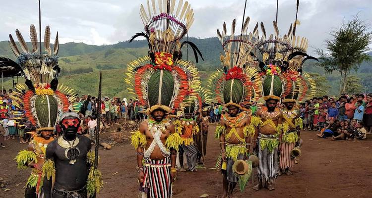 Personas con trajes tradicionales actuando en una reunión pública; montañas al fondo.