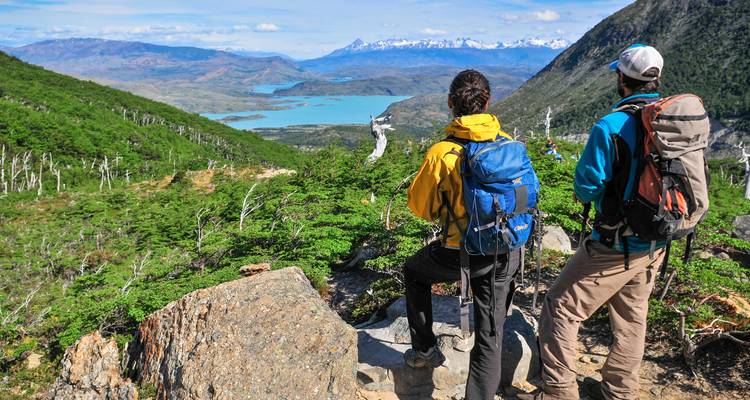 Deux routards font une pause à un belvédère panoramique surplombant des lacs turquoise et des chaînes de montagnes enneigées au loin en Patagonie.