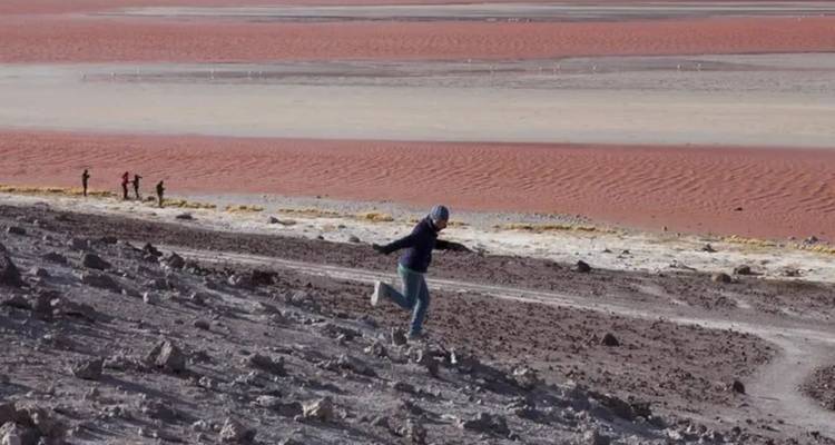 Persona corriendo por una colina rocosa con una laguna roja de fondo.