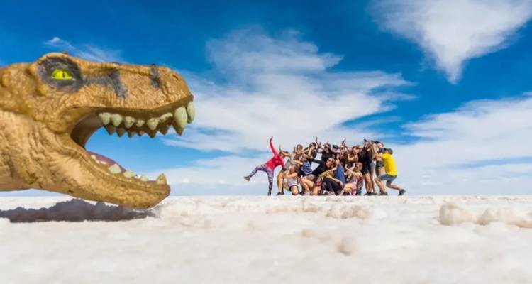 Grupo de personas posando de manera divertida en un salar con un dinosaurio de juguete en primer plano.