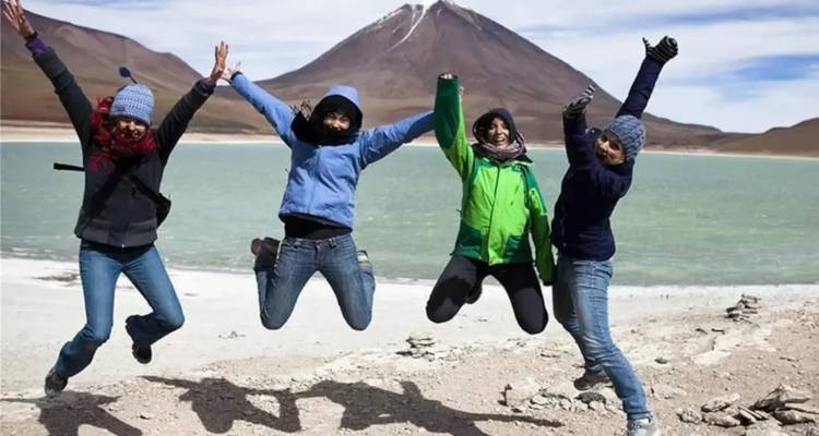 Cuatro personas saltando alegremente junto a un lago con montañas de fondo.
