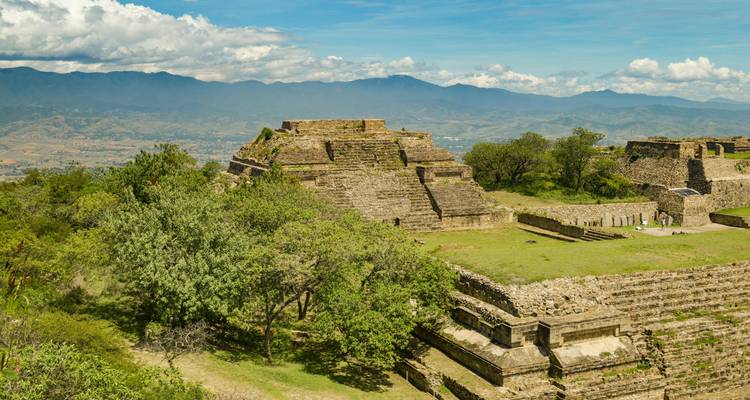 The terraced stone ruins of Monte Albán sit atop a hill overlooking the valleys of Oaxaca under a bright sky.