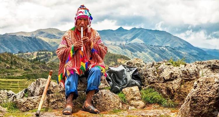 Persona tocando un instrumento tradicional con un paisaje montañoso de fondo.
