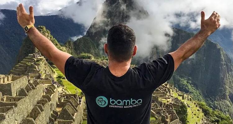 Persona con los brazos levantados frente a Machu Picchu.