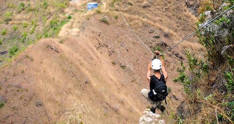 Una persona deslizándose en tirolesa sobre una zona montañosa y árida.