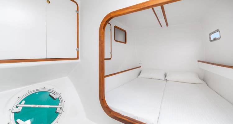 Poste d'amarrage de yacht avec matelas jumeaux, hublot rond et intérieur nautique blanc.