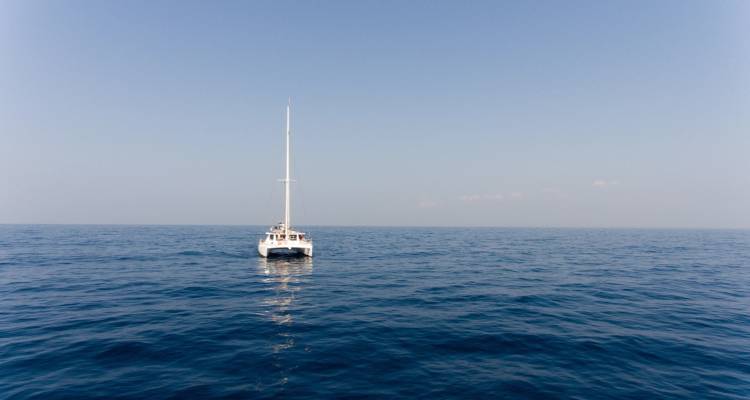 Catamaran à voile solitaire sur une vaste mer calme sous un ciel dégagé.