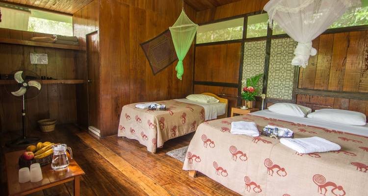 Simple twin room in a jungle lodge with wooden walls, mosquito nets and neatly folded towels.