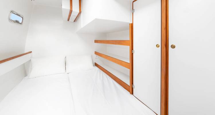 Cabine de yacht simple avec lit double et étagères en bois.