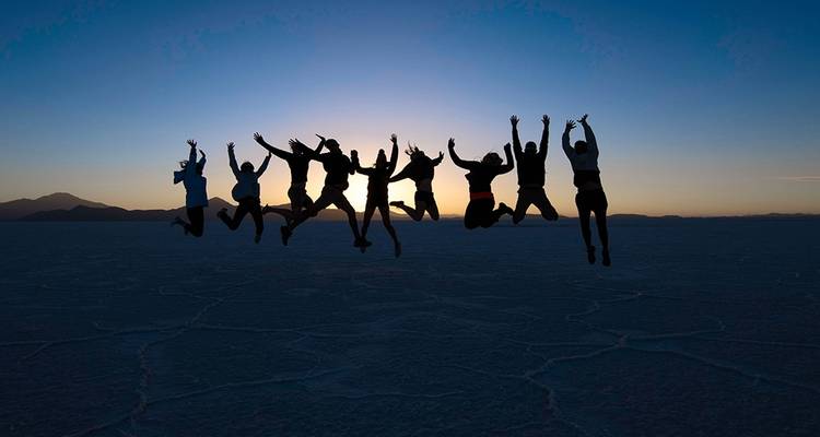 Grupo en silueta saltando en el aire al atardecer sobre el Salar de Uyuni.