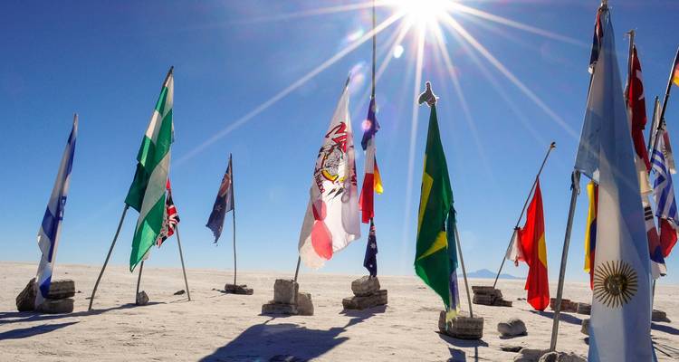 Varias banderas internacionales plantadas en el Salar de Uyuni bajo un sol brillante.