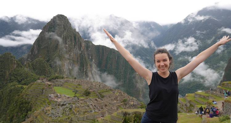 Persona posando con los brazos extendidos frente a Machu Picchu.