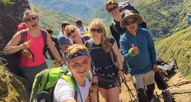 Group selfie of hikers on a hillside with a scenic view in the background.
