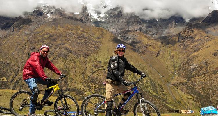 Two cyclists in mountainous terrain with cloudy peaks in the distance.