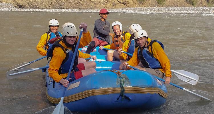 Group of people on a raft in a river wearing yellow jackets and helmets.
