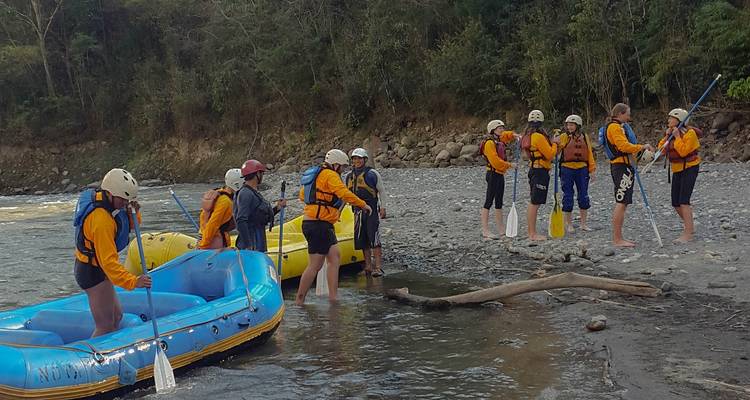 Rafting group preparing to enter the river, some standing on the riverbank.
