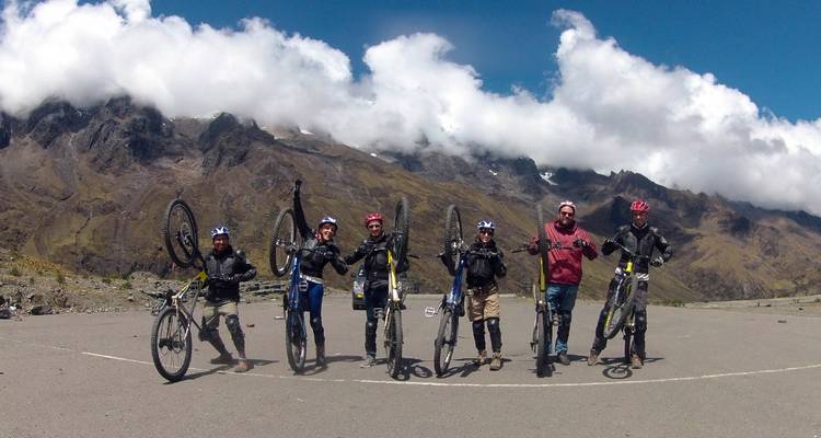 Group of cyclists posing with their bikes against a mountainous backdrop.