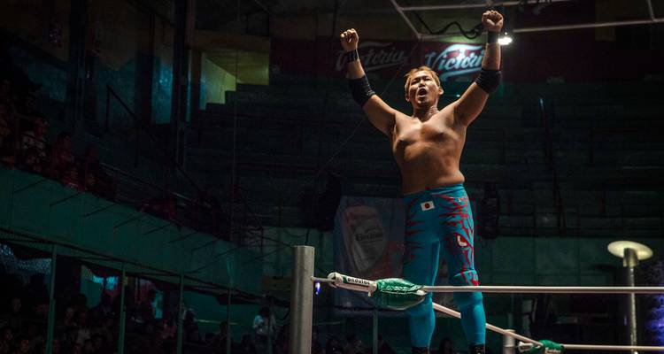 Luchador de lucha libre en un ring celebrando bajo las luces de la arena.