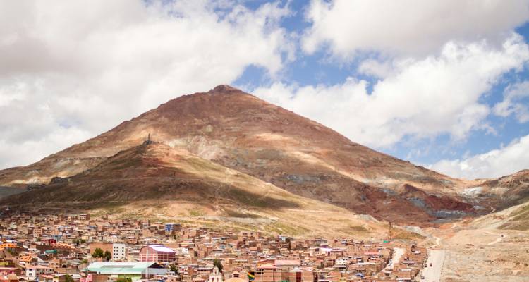 Una montaña con un pequeño pueblo en su base bajo un cielo parcialmente nublado.