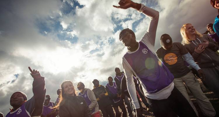 Un groupe animé de porteurs et de trekkeurs dansant et applaudissant sous un ciel radieux, célébrant sur un sentier de montagne.