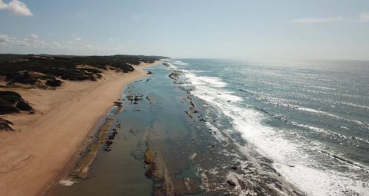 Luftaufnahme eines Strandes mit Wellen und felsiger Küste.