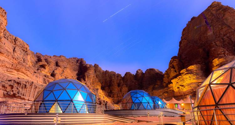 Domos de cristal futuristas de un campamento desértico ubicado entre los imponentes acantilados de Wadi Rum bajo un cielo crepuscular estrellado