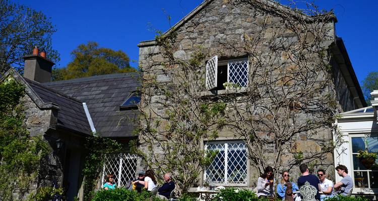 Une charmante maison en pierre avec des gens assis dehors profitant d'une journée ensoleillée.