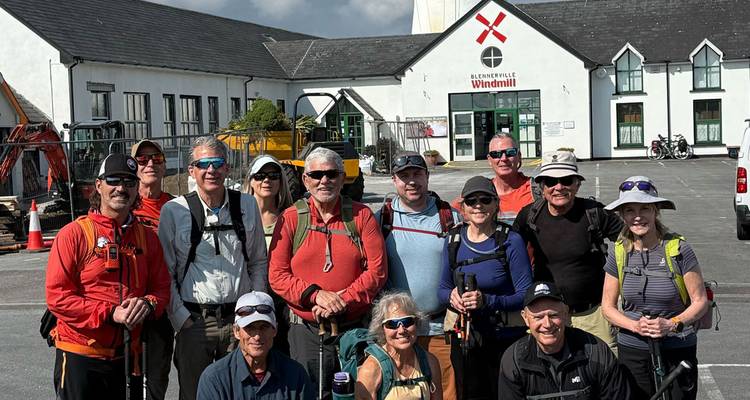 A group posing in front of a windmill, holding trekking poles.