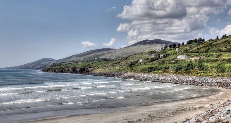 Plage et collines ondulantes sous un ciel partiellement nuageux.