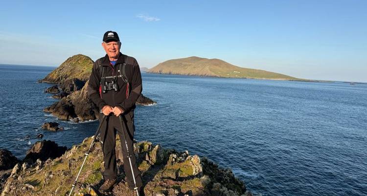 Un randonneur solitaire debout sur des rochers côtiers, face à l'océan.