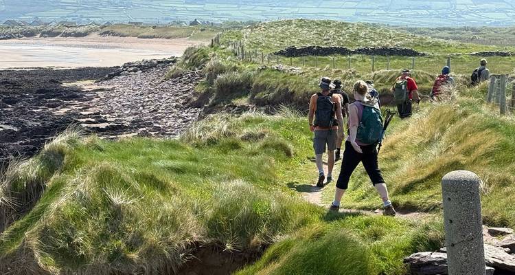 Des randonneurs marchant le long d'un sentier côtier, avec des vues sur la plage et la mer.