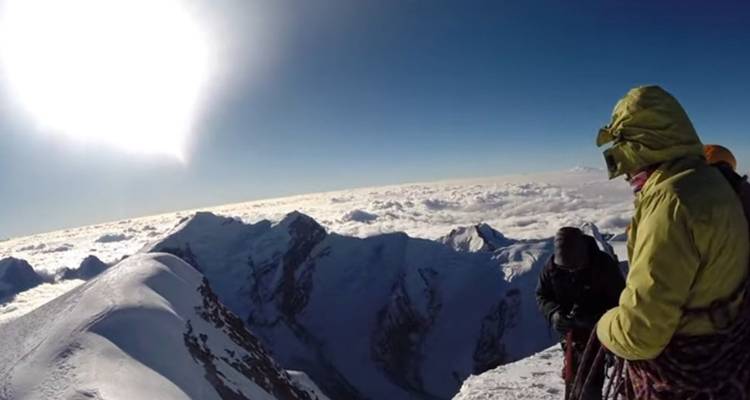 Des randonneurs sur un sommet enneigé avec un soleil éclatant.