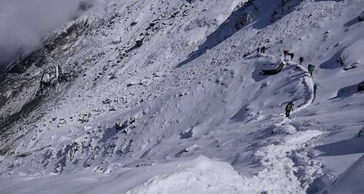 Des randonneurs marchant le long d'un sentier de montagne enneigé.