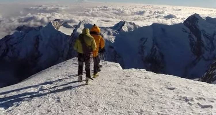 Zwei Personen, die einen verschneiten Berg mit Wolken in der Ferne besteigen.