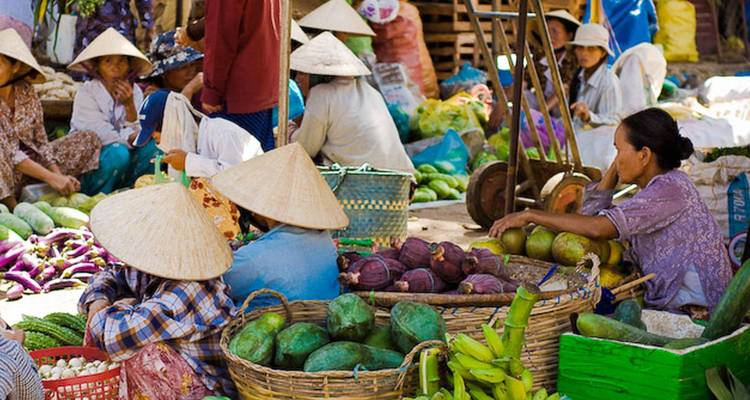 Escena de mercado con vendedores y productos tradicionales, personas usando sombreros cónicos.