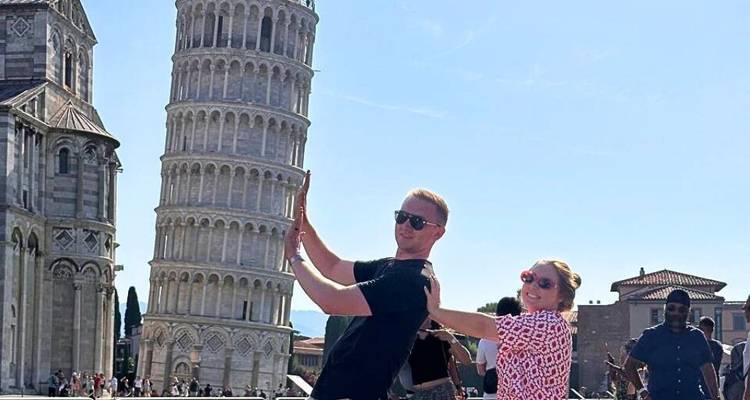Ein Paar posiert verspielt vor dem Schiefen Turm von Pisa.