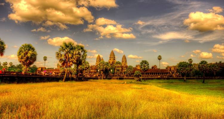 Complexe du temple d'Angkor Vat avec des palmiers et un ciel vibrant.