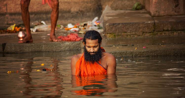 Un homme vêtu d'orange se tenant dans l'eau, participant peut-être à un rituel.