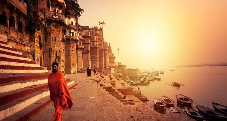 Personne en tenue traditionnelle sur des marches au bord de la rivière au coucher du soleil.