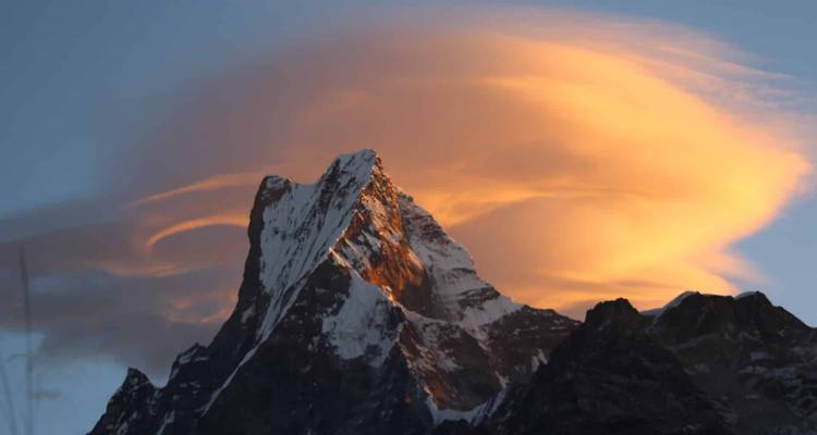Snow-capped mountain peak with golden clouds at sunrise.