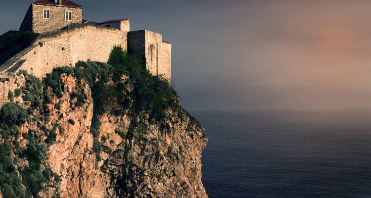 Vue panoramique sur l'océan avec un fort historique sur une falaise au coucher du soleil.
