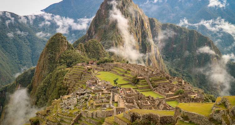 Vue iconique du Machu Picchu avec des nuages flottant autour des sommets.