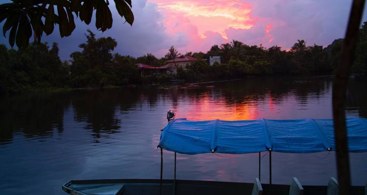 Scène fluviale sereine au crépuscule avec des nuages roses et violets se reflétant à côté d'un bateau recouvert d'une bâche bleue vide